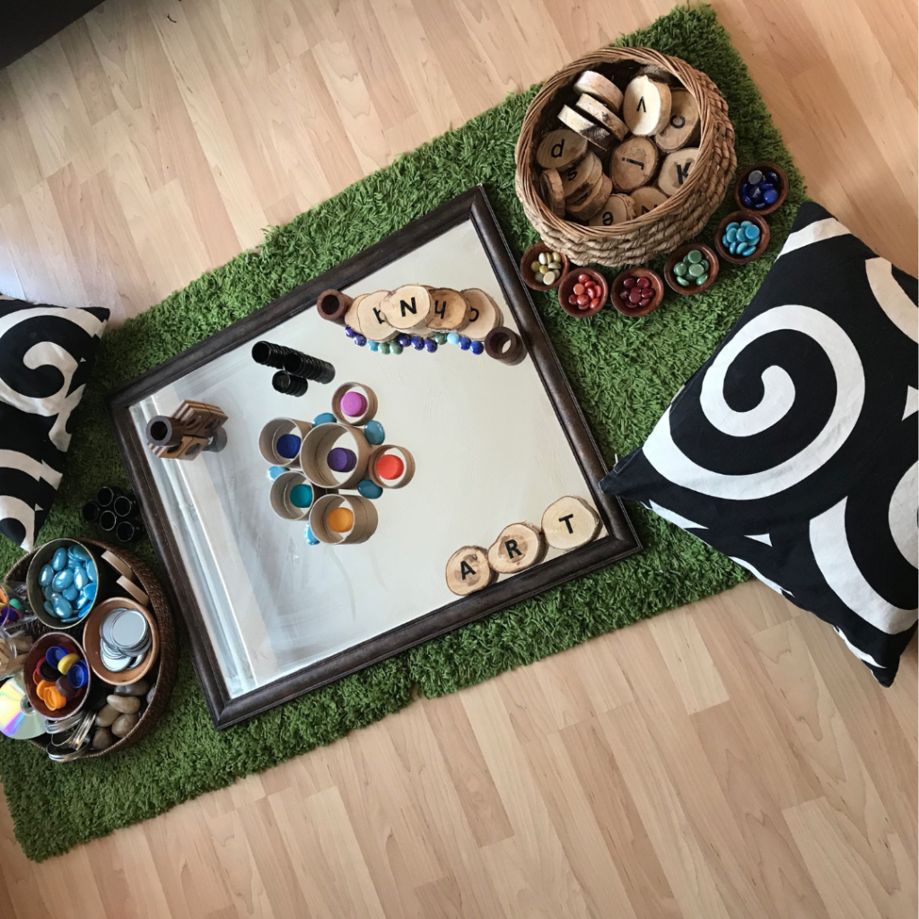 Transient Art Invitation To Play on the floor with large glass mirror, pillows and loose parts.