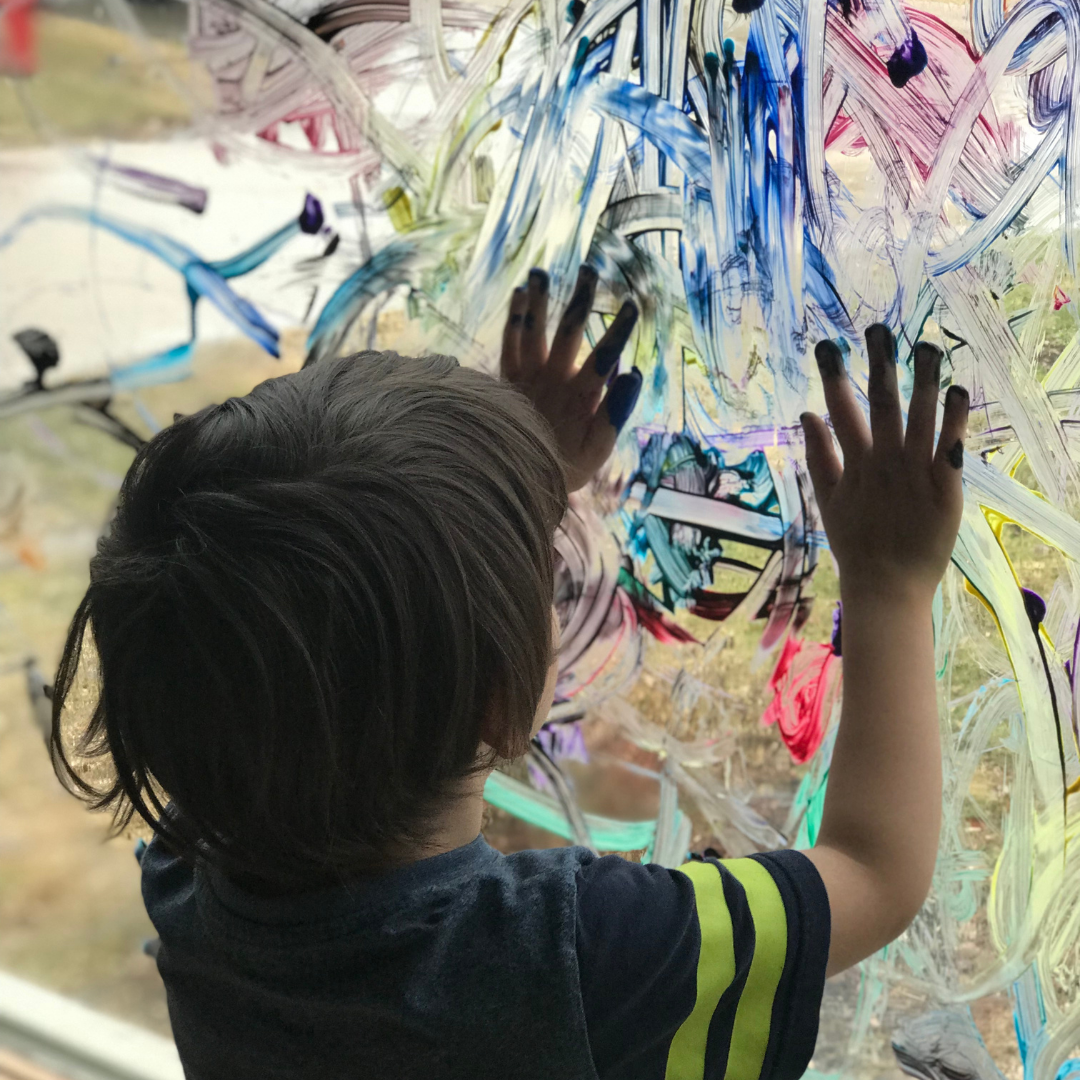 Child painting with hands on a window to showcase image of the child within the Reggio Emilia Approach